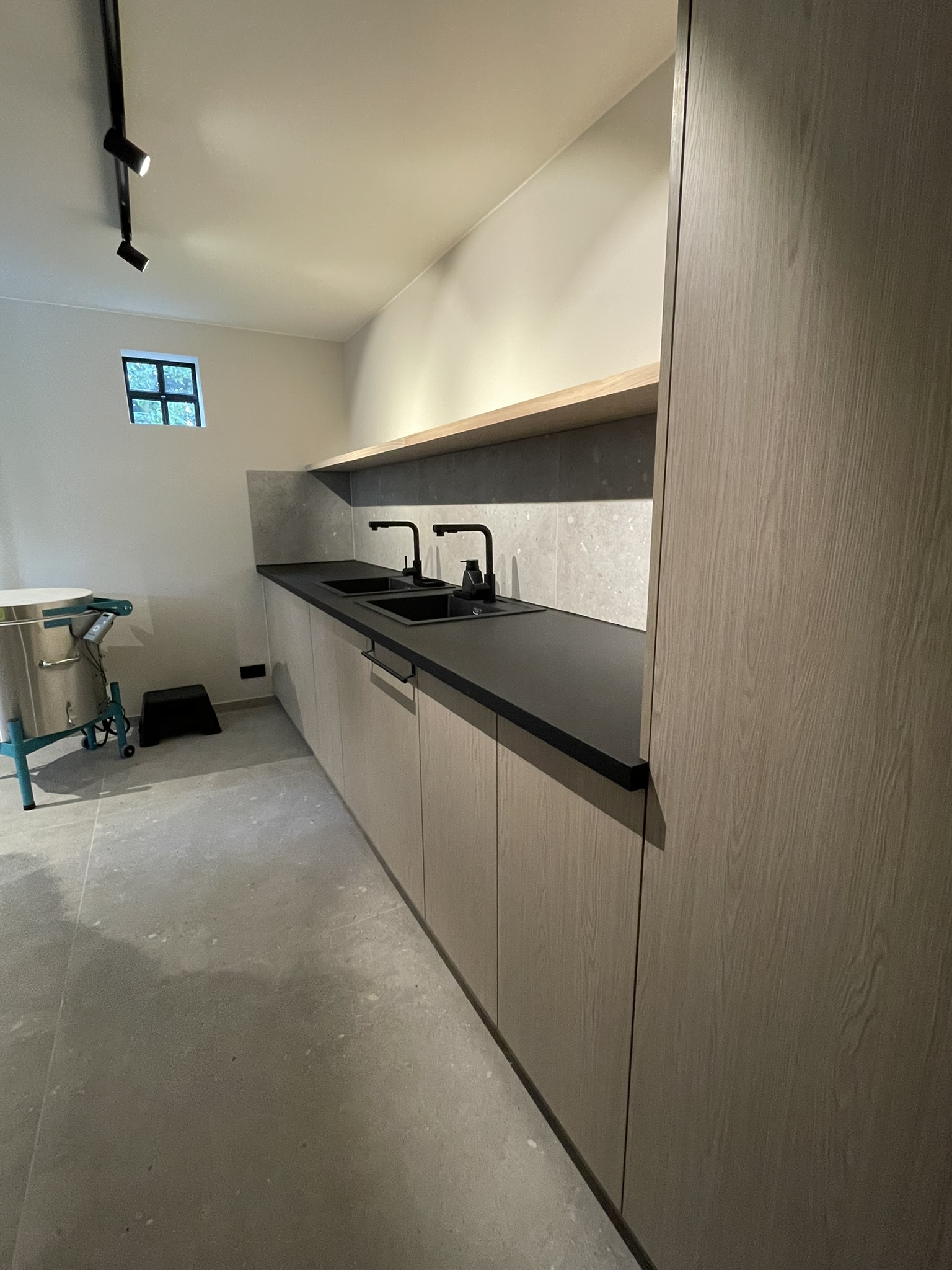 Kastenwand in melamine houtdecor met zwart werkblad en spoelbakken, naast de keramiekoven in het atelier