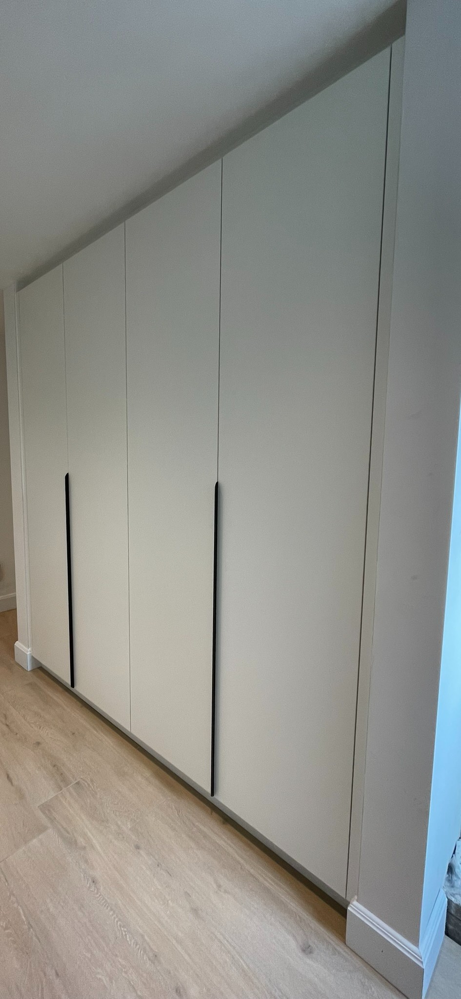 Witte kastenwand met lange zwarte grepen, vlak en rustig over de volledige muur